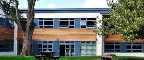 A blue, white and brown modular school building with a green lawn and picnic benches in front.